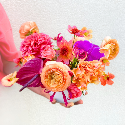 Vibrant bouquet of coral garden roses, hot pink dahlias, magenta zinnias, and orange ranunculus arranged in a loose, modern style.
