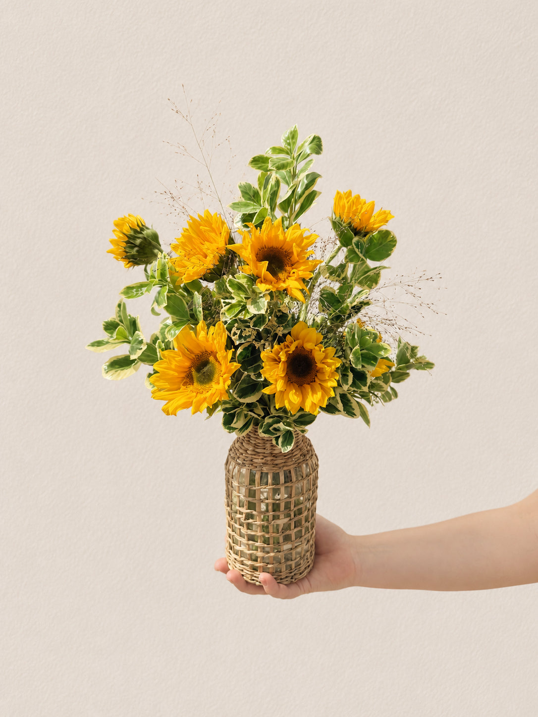 Signature sunflower arrangement with ten sunflowers and lush greens in a tall wicker bottle-neck vase