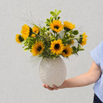 Luxe sunflower arrangement with sixteen sunflowers and greenery in a large wavy ceramic vase