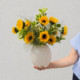 Luxe sunflower arrangement with sixteen sunflowers and greenery in a large wavy ceramic vase