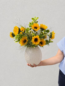 Luxe sunflower arrangement with sixteen sunflowers and greenery in a large wavy ceramic vase