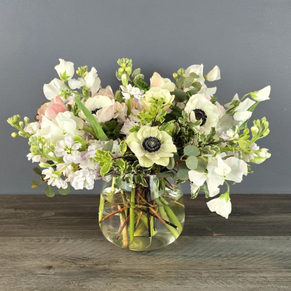 A floral arrangement featuring anemones, tulips, and stock in shades of white and pink, presented in a clear glass vase.