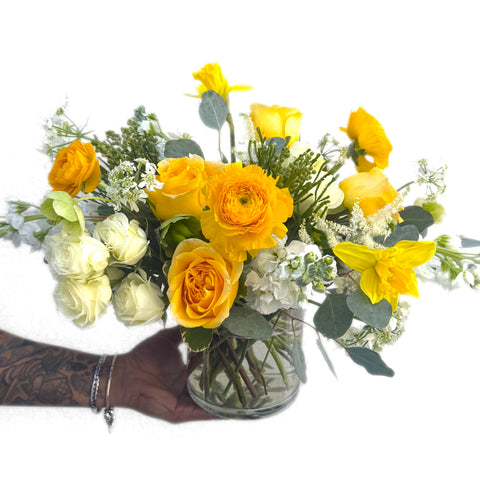 Yellow roses and daffodils arranged with white ranunculus and greenery in a clear glass vase. — The Flower Bar, Larchmont NY