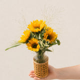 Mini Soleil sunflower arrangement with five golden sunflowers and airy grasses in a small wicker bottle-neck vase