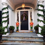 Elegant front entrance decorated with cascading garland swags, festive nutcracker statues, and poinsettia planters flanking a black door.