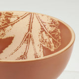 Terracotta ceramic bowl with pressed botanical branch design in rust tones.