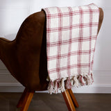 A red and cream plaid throw blanket drapes over a brown mid-century modern chair with wooden legs.