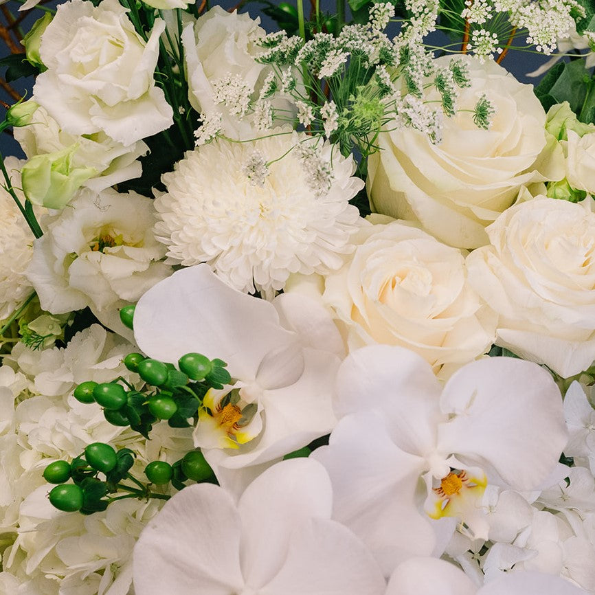Luxurious bridal bouquet featuring white orchids, cream roses, white peonies, and baby's breath with lush green foliage.