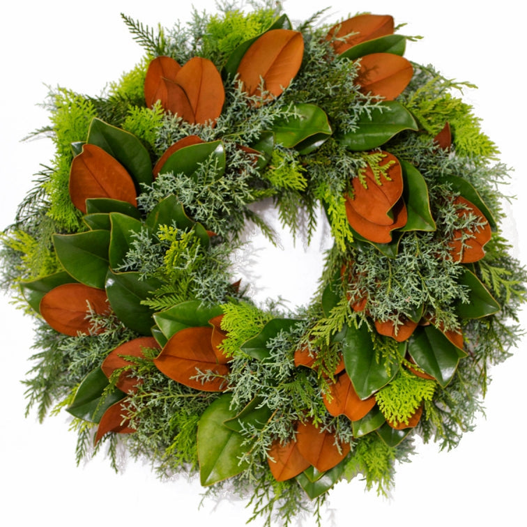 A lush evergreen wreath adorned with orange physalis, green magnolia leaves, and white-dusted frosty greenery arranged in a full circular design.