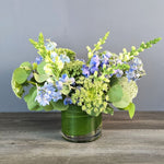 Blue hydrangeas, white snapdragons, and chartreuse queen Anne's lace in a green cylinder vase with eucalyptus foliage.