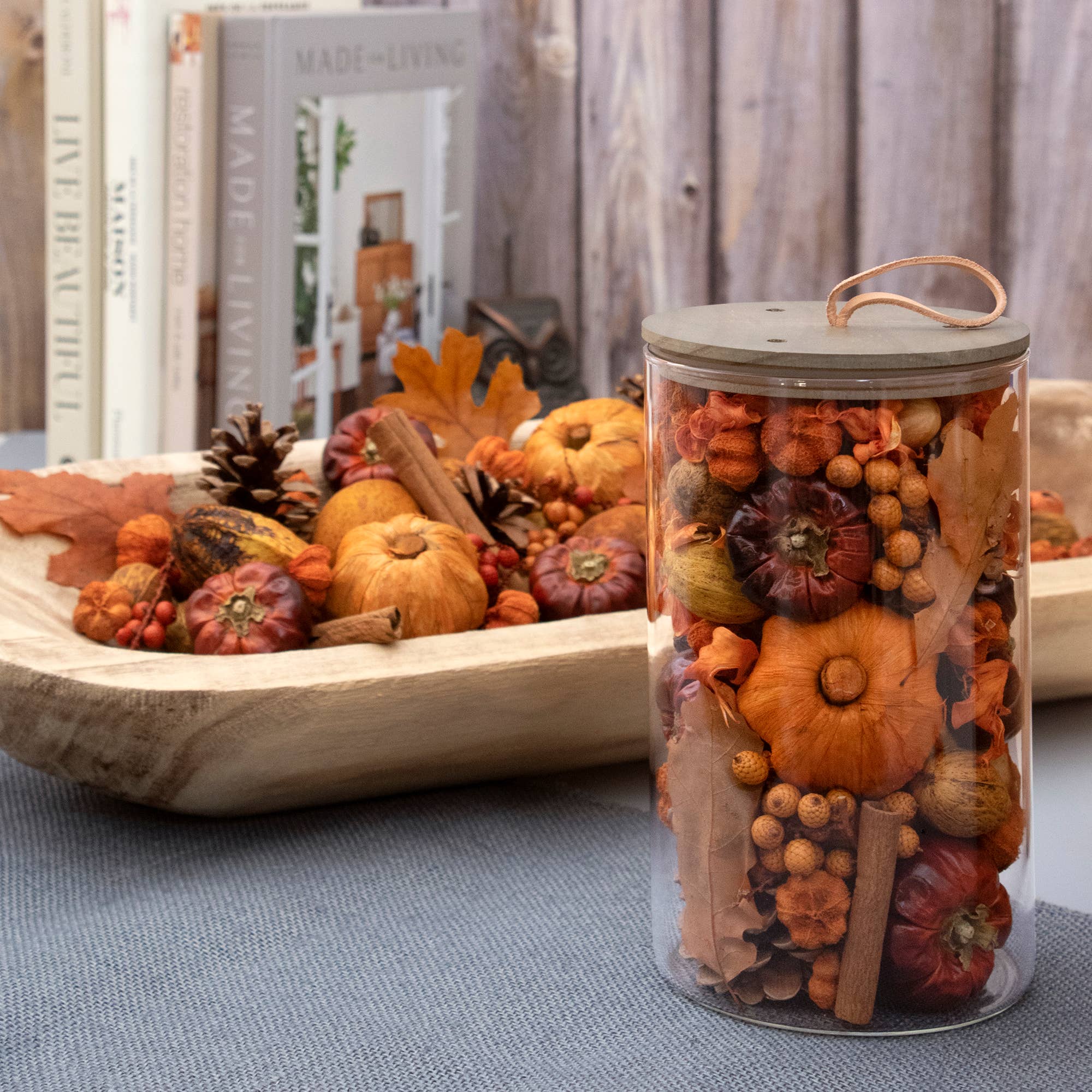 Autumn decorative arrangement featuring orange and burgundy miniature pumpkins and gourds displayed in a clear cylindrical container with wooden handle.