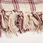 Close-up of burgundy and cream fringed textile edge with geometric woven pattern detail.