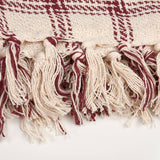 Close-up of burgundy and cream fringed textile edge with geometric woven pattern detail.