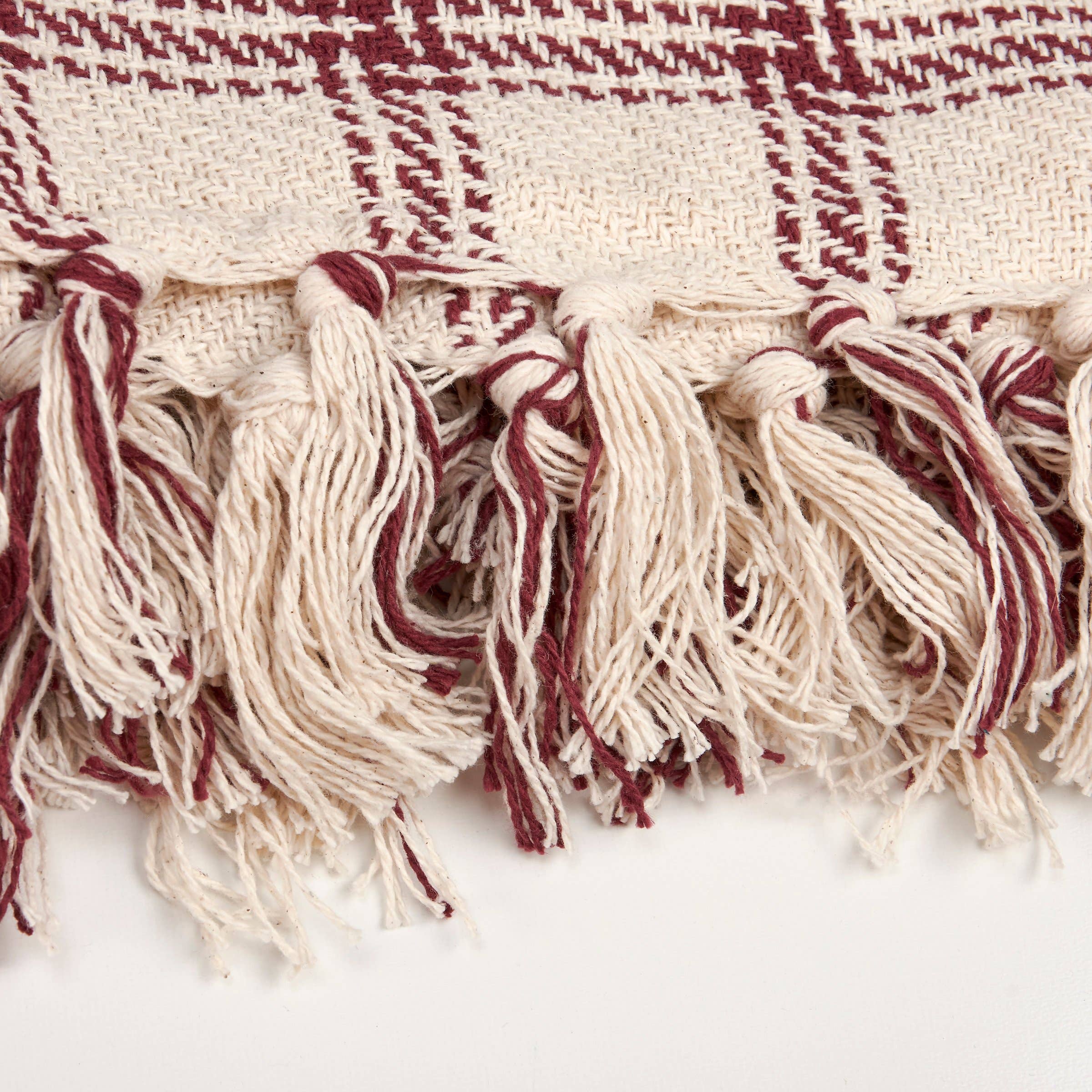 Close-up of burgundy and cream fringed textile edge with geometric woven pattern detail.