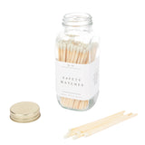 A glass jar of safety matches with a cream-colored lid and white label, displayed with several wooden matchsticks beside it.