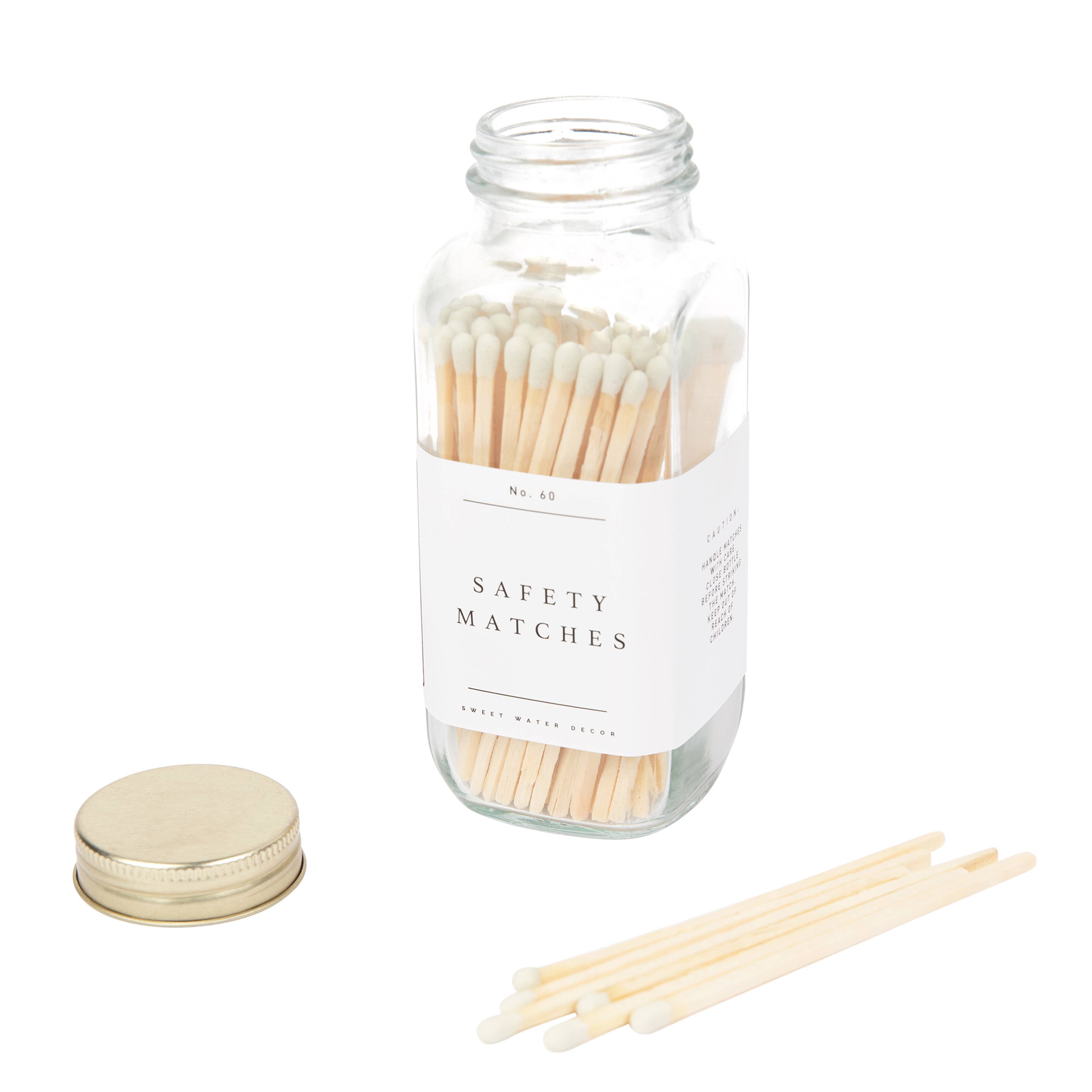 A glass jar of safety matches with a cream-colored lid and white label, displayed with several wooden matchsticks beside it.