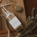 A glass jar of safety matches with a white label sits on a wooden surface next to green dried celosia stems.