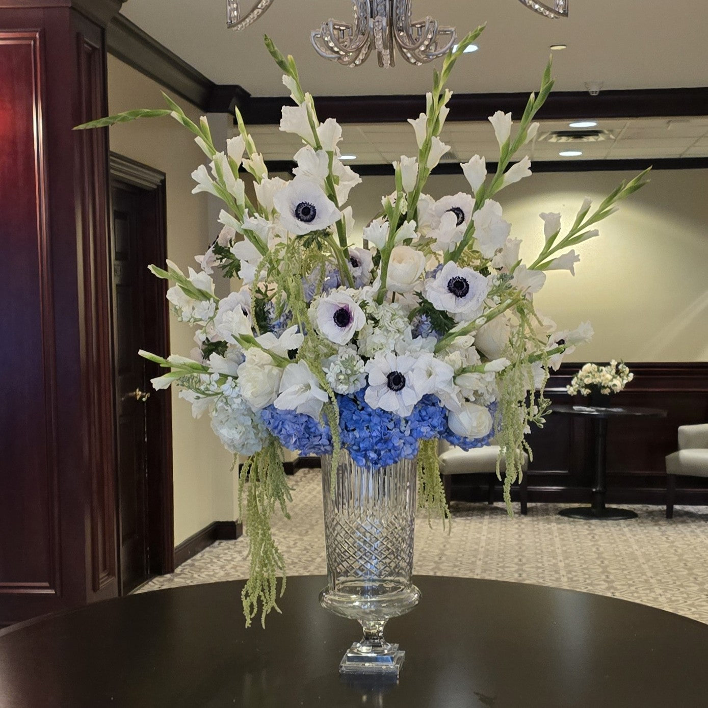 Placecard table arrangement with white anemones, gladiolus, and blue hydrangeas in a crystal urn by The Flower Bar, Westchester wedding florist